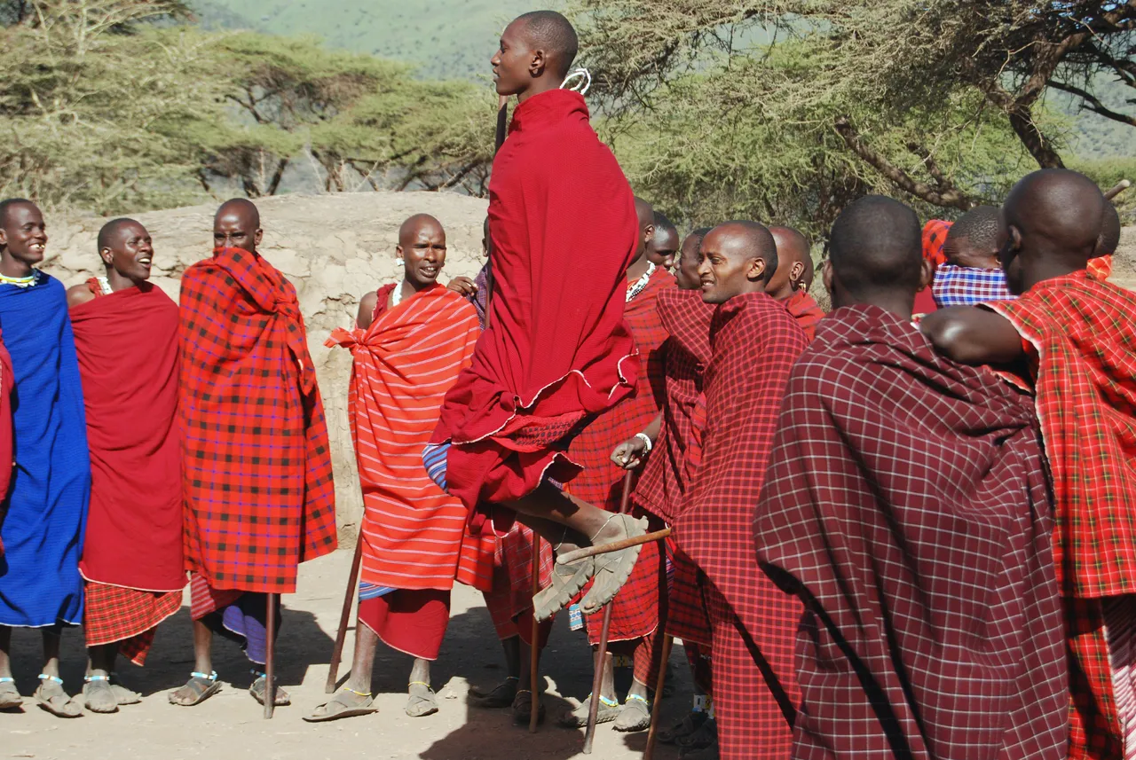A Maasai man mid-jump during the adumu, surrounded by others in red shukas
